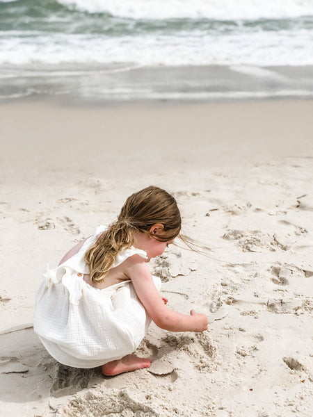 Girl playing in the sand while wearing our signature double gauze cross back ruffle dress in the color shell.