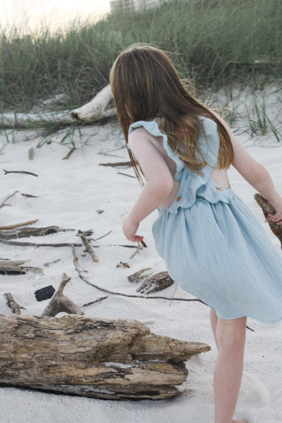 Girl exploring the beach in our signature double gauze cross back ruffle dress in the color Seafoam.