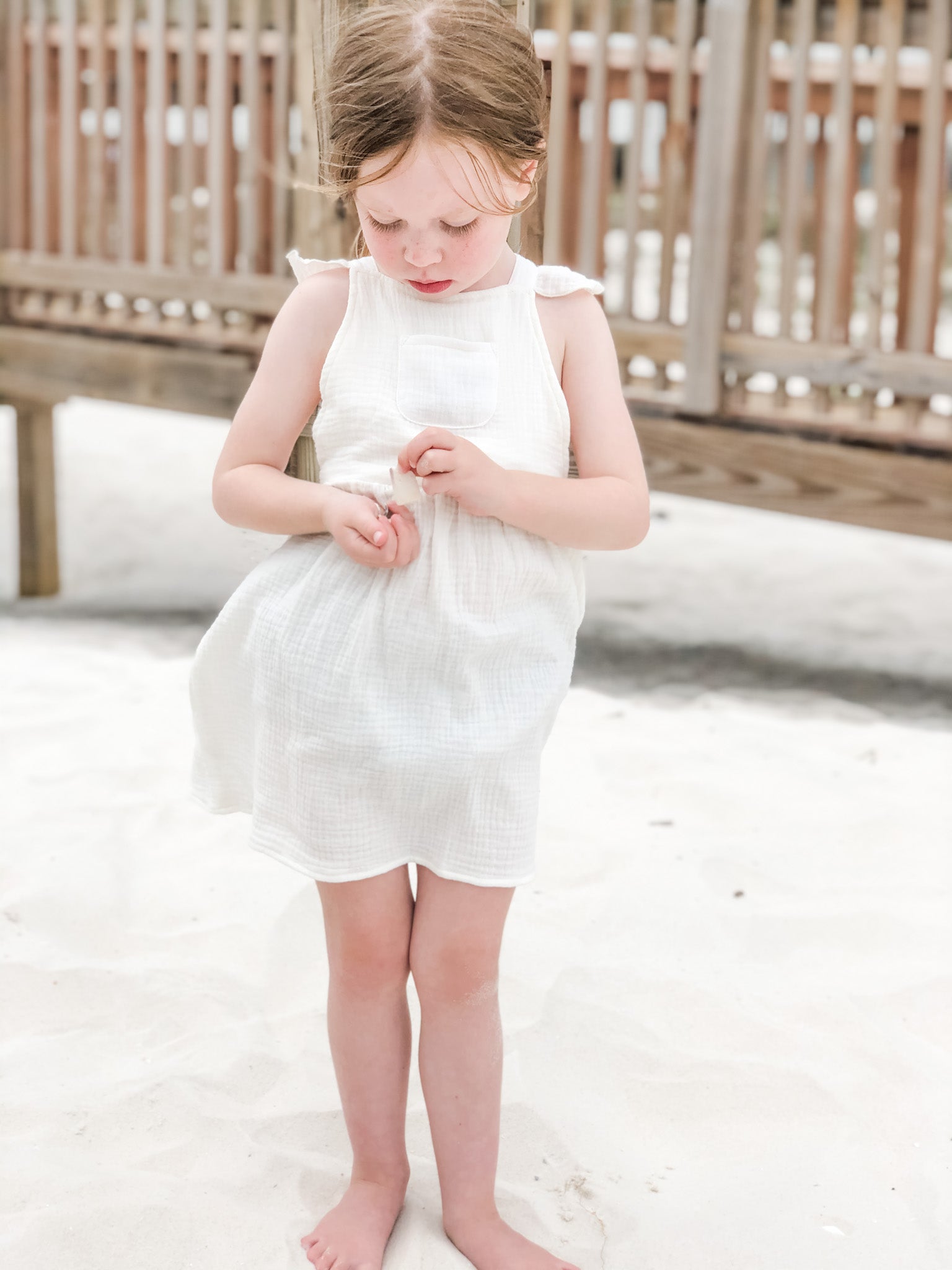 Girl playing with shells while wearing our signature double gauze cross back ruffle dress in the color shell.